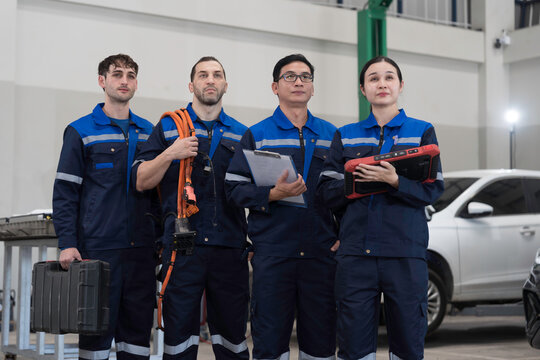 Electric vehicle car auto services, EV garage. Team of mechanic and electrician standing wear work uniform and holding equipment tools for work in auto workshop