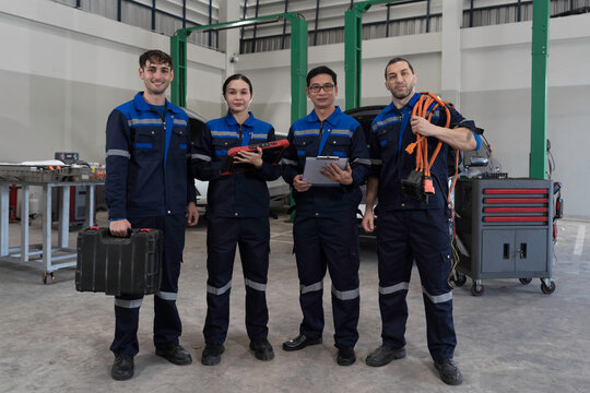 Electric vehicle car auto services, EV garage. Team of mechanic and electrician standing wear work uniform and holding equipment tools for work in auto workshop