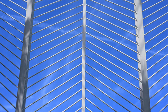 decorative arching open web exterior structural steel frame. curved I beams and diagonal round or circular section bracing members. perspective view looking up. crisp blue sky background.    