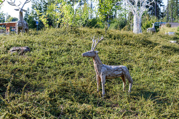 Naklejka premium Artistic driftwood deer sculpture standing on a lush green hill in a beautiful outdoor park setting.