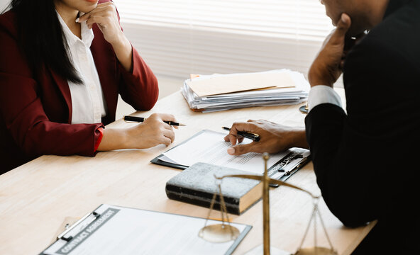 Legal Consultation: Two professionals sit at a desk, carefully reviewing and signing legal documents. In the background a scale of justice rests, and a gavel sits nearby.	