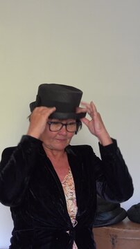 Woman adjusts a retro black hat while standing indoors. vertical video.