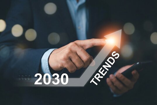 Businessman touching glowing upward pointing arrow with text 2030 trends on dark background