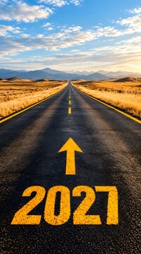 Year 2027 painted on an empty asphalt road leading into the distance with a bright yellow arrow pointing forward towards the horizon under a beautiful sunset sky and open landscape