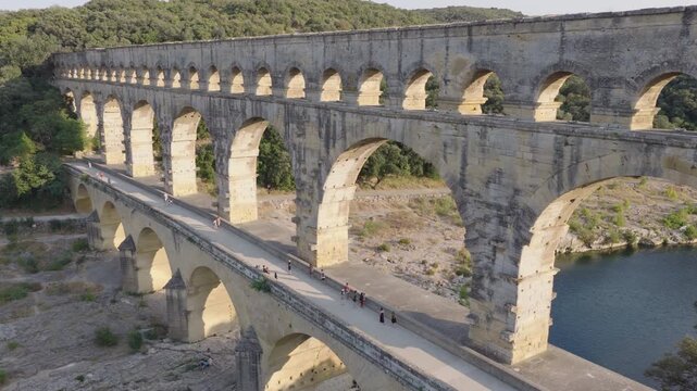Close aerial of Pont du Gard walkway with tourists over river and limestone banks