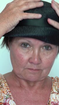 A woman is holding her black hat on her head. vertical video.