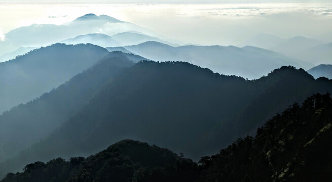 View of the layered peaks of Tacana Volcano shrouded in morning mist with dense forest in the foreground in Chiapas, Mexico.