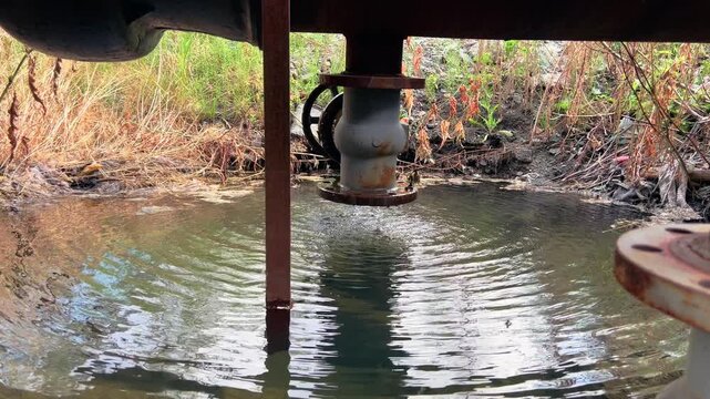 Abandoned industrial valve and support reflected in shallow stagnant water