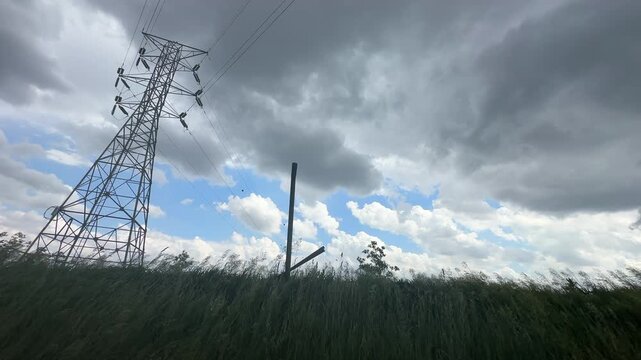 Low angle view of storm clouds and wind over a field with a high voltage transmission tower to the side in a rural area of the midwest USA 