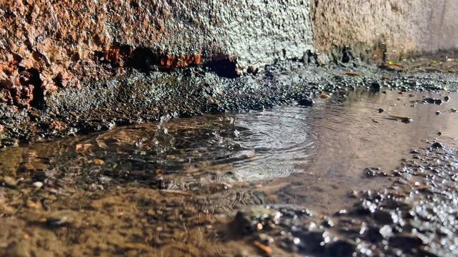 Rainwater forms overlapping ripples across puddle beside old masonry wall