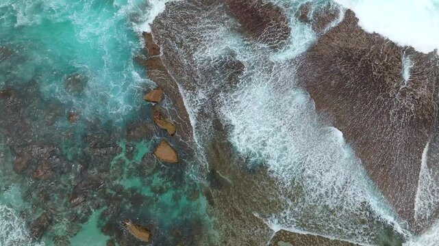 Aerial view of turquoise ocean waves crashing against the rocky shore and jagged cliffs at Salmon Holes in Albany, Western Australia, Australia.