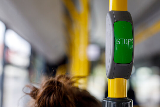 Close-up of a green stop request button on a yellow pole inside a public bus or tram.