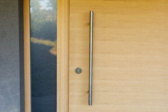 Close-up of a contemporary wooden entrance door with a sleek metal pull handle and keyhole.