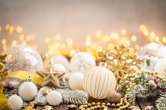 A Christmas background featuring elegant white and silver baubles, glittering stars, jingle bells, and snowflakes on rustic wood, set against a warm backdrop with twinkling lights and copy space.