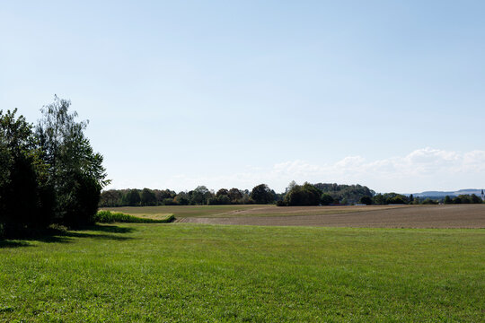 Scenic view of green grass, cultivated fields, a line of trees, and a distant village under a clear