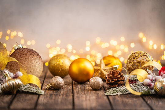 A Christmas background featuring warm gold baubles, a glittering snowflake, star, and pinecone arranged on rustic wood, set against a soft backdrop with twinkling lights and copy space.