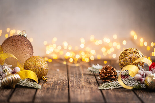 A Christmas background featuring warm gold baubles, a glittering snowflake, star, and pinecone arranged on rustic wood, set against a soft backdrop with twinkling lights and copy space.