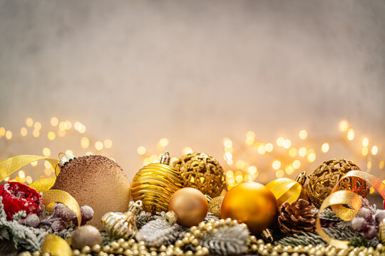 A Christmas background featuring warm gold baubles, a glittering snowflake, star, and pinecone arranged on rustic wood, set against a soft backdrop with twinkling lights and copy space.