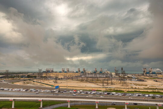 View of the DEWA power plant with industrial smokestacks and power lines under a stormy sky, with highway traffic in the foreground, Dubai, Dubai, United Arab Emirates.