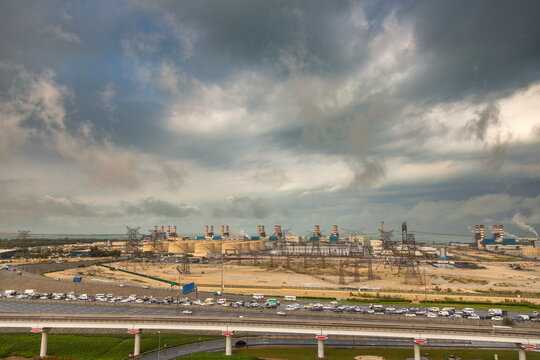 View of the Dubai Electricity and Water Authority power plant with industrial cooling towers, power lines, and a busy highway under a dramatic cloudy sky in Dubai, Dubai, United Arab Emirates.