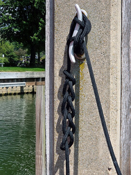A black rope is hanging on a dock cleat, intricately braided in a unique design