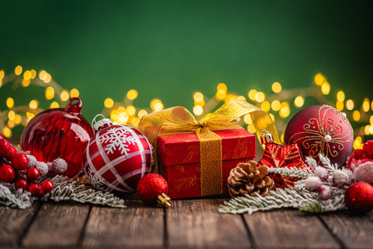 A Christmas background featuring an abundant arrangement of red baubles, a glittering star, and a pinecone nestled in frosted pine on rustic wood, set against green with twinkling lights.
