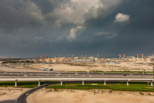 View of the Dubai Electricity and Water Authority power plant with industrial infrastructure, highway traffic, and metro line under a stormy sky in Dubai, Dubai, United Arab Emirates.