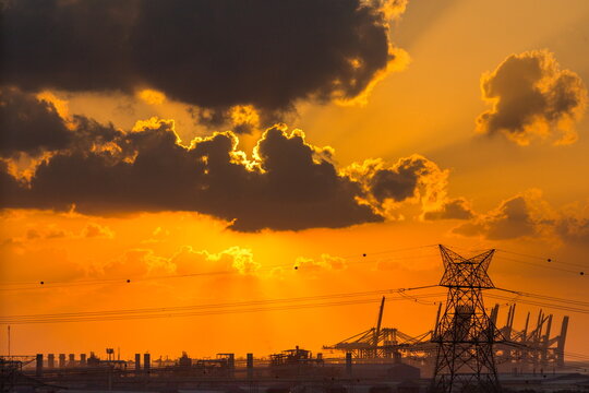 View of an industrial area with power lines and cranes silhouetted against a vibrant sunset sky in Dubai, Dubai, United Arab Emirates.