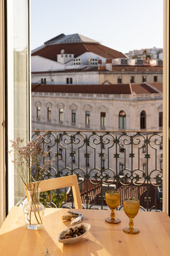 amber gold vintage goblet wine glass and olives on a table next to linen napkin and wine opener with balcony and city views in late afternoon with glass vase of wildflowers 