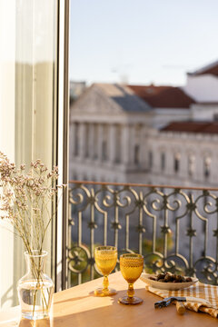 amber gold vintage goblet wine glass and olives on a table next to linen napkin and wine opener with balcony and city views in late afternoon with glass vase of wildflowers 