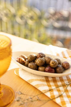 garnished olives in ceramic bowl on linen napkin with goblet in the foreground and balcony with city views in the background 