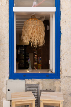 street view of blue trim window of small restaurant in Lisbon, Portugal with large rattan lamp and two stools outside