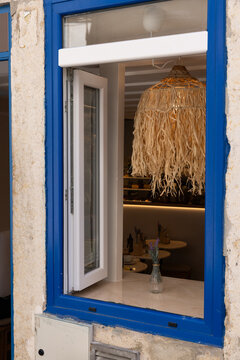 street view of blue trim window of small restaurant in Lisbon, Portugal with large rattan lamp and two stools outside