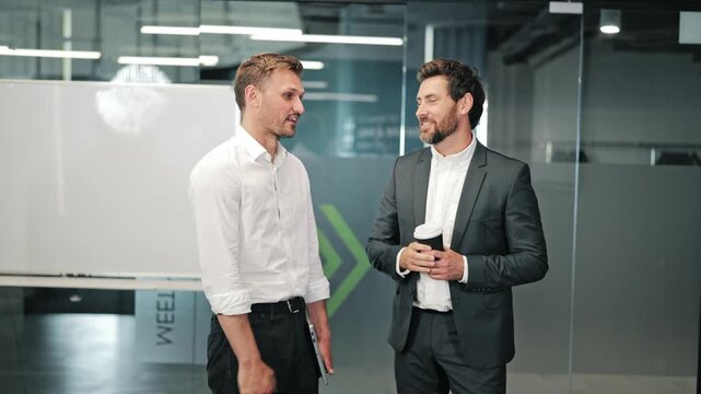 Professional men shake hands, engage in discussion. Conversation unfolds in contemporary office, featuring collaboration and shared ideas. Corporate interaction and successful communication shown.