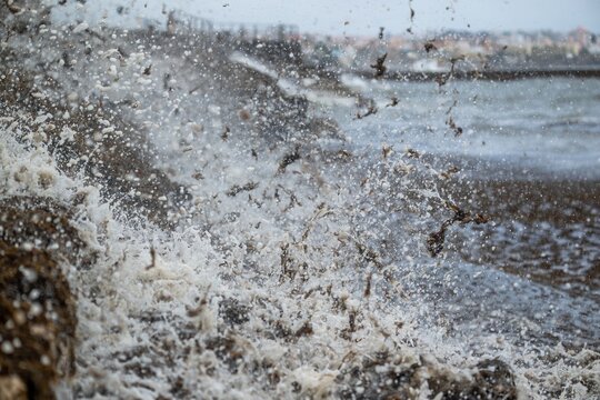 View of powerful ocean waves crashing against the rocky coastline, creating a dramatic storm surge with sea foam and scattered seaweed in Cascais, Lisbon, Portugal.