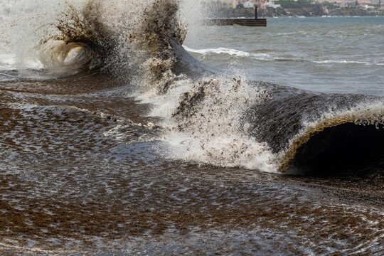View of a powerful storm surge crashing onto the shore, carrying large amounts of dark seaweed across the water in Cascais, Lisbon, Portugal.