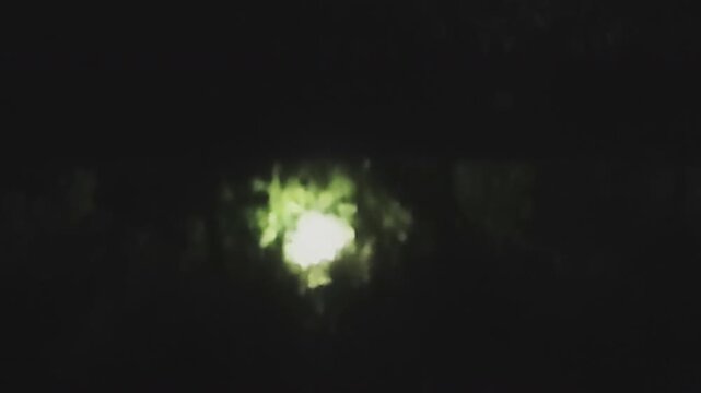 Spooky and mysterious night scene with a bright light reflecting on the rippling surface of water, seen through foliage in the dark