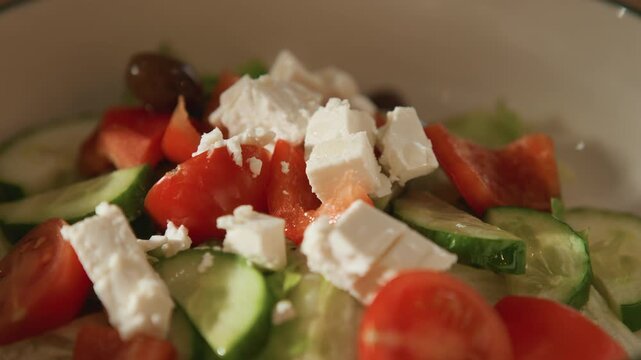 Close up of fresh salad ingredients including tomatoes cucumbers olives and feta cheese in bowl. scene focuses on vibrant colors and textures as each ingredient is added to create greek