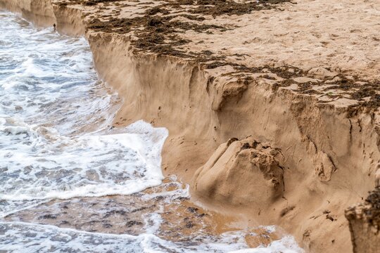 View of coastal erosion on a sandy beach with waves crashing against the sand cliff in Cascais, Lisbon, Portugal.