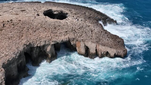 coral lagoon headland malta blowhole sinkhole punctures limestone rock sea caves arches undercut base waves crash turquoise water aerial orbit drone footage natural erosion formation coastal geology