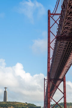View of the red steel structure of the Ponte 25 de Abril bridge with the Cristo Rei statue visible in the distance in Lisbon, Lisbon, Portugal.