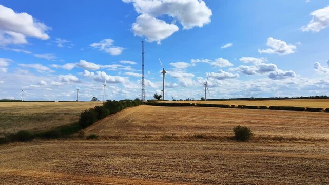 Aerial view of Burton Wold wind farm with rotating wind turbines set against golden harvested fields and a blue sky in Burton Latimer, England, United Kingdom.