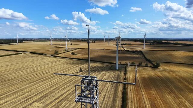 Aerial view of Burton Wold wind farm with large wind turbines standing in golden harvested wheat fields under a blue sky in Burton Latimer, England, United Kingdom.