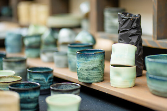 Handmade ceramic cups, bowls and vases displayed for sale at an outdoor craft market. Artisan pottery with unique glazes represents traditional craftsmanship and local small business.
