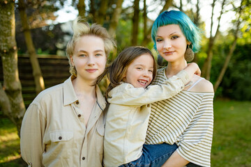 Fototapeta premium Three siblings pose together outdoors on a warm autumn day, with a smiling boy hugging his older sister. Natural family portrait in a garden setting.