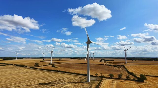 Aerial view of wind turbines at Burton Wold wind farm in golden harvested fields under a blue sky with white clouds in Burton Latimer, England, United Kingdom.