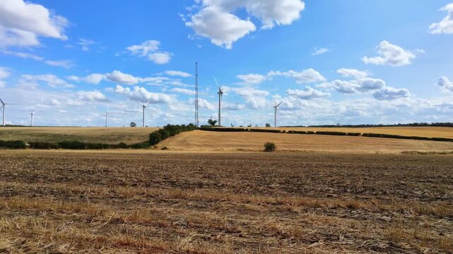 Aerial view of the wind turbines at Burton Wold wind farm set against a blue sky with fluffy clouds over the agricultural fields of Burton Latimer, England, United Kingdom.
