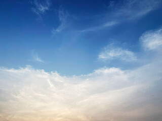 Obraz premium Serene blue sky with soft wispy white clouds illuminated by warm sunlight near the horizon