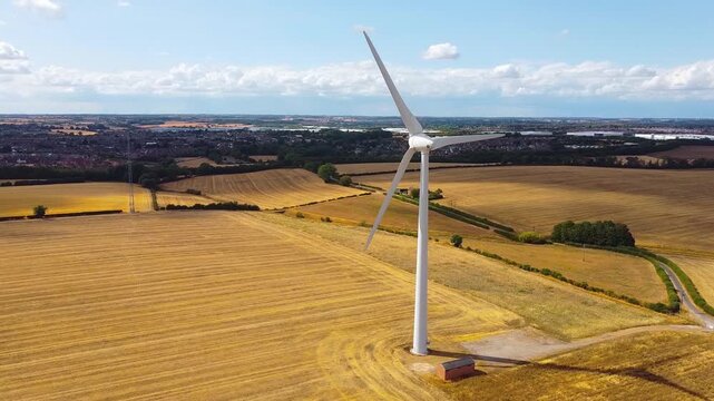 Aerial view of Burton Wold wind farm turbine 1 standing in golden harvested fields under a blue sky in Burton Latimer, England, United Kingdom.