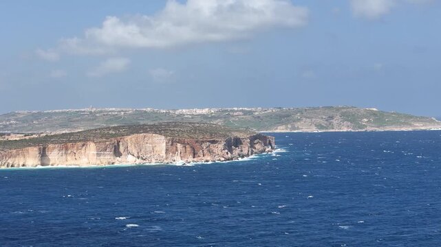 layered limestone cliffs malta rise above turquoise cove sandy beach coastal watchtower stands hilltop distant town sprawls horizon mediterranean sea aerial panorama wide scenic coastline view